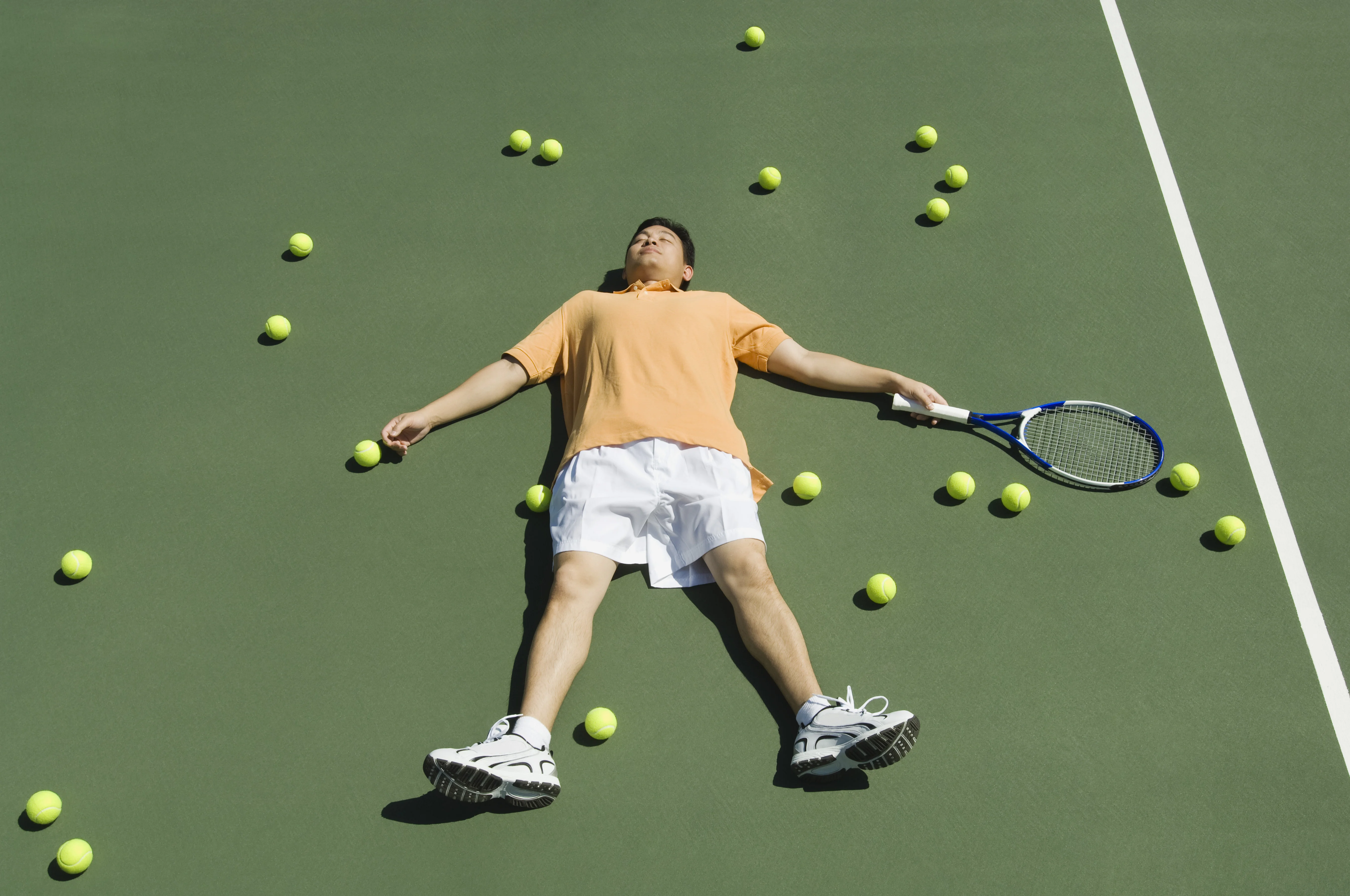 Tennisspeler liggend tussen tennisballen